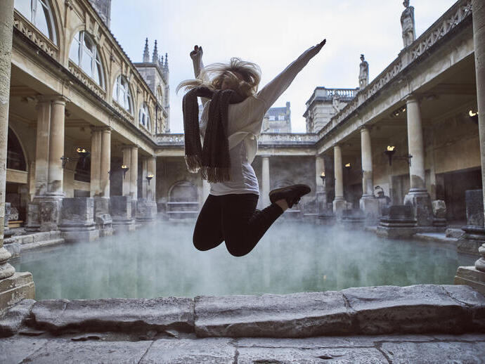 Woman leaping in the air at The Roman Baths, Bath, Somerset, England.