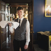 Member of staff holding a tray with two glasses of wine in a restaurant