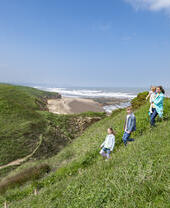 Une famille marche sur une colline herbeuse surplombant la plage et la mer sous un ciel bleu.