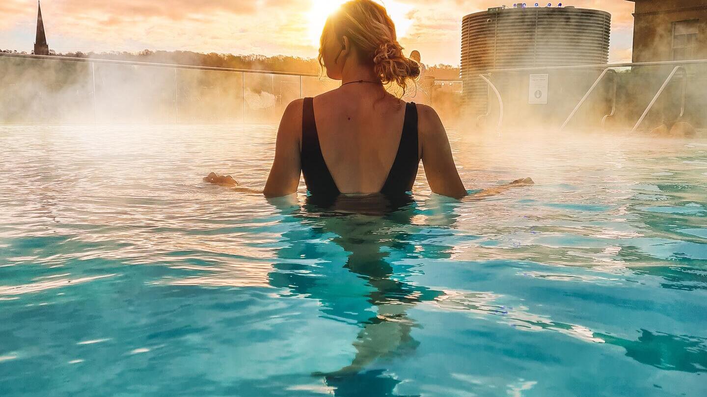 A woman stands looking out to a view in the rooftop pool at sunrise