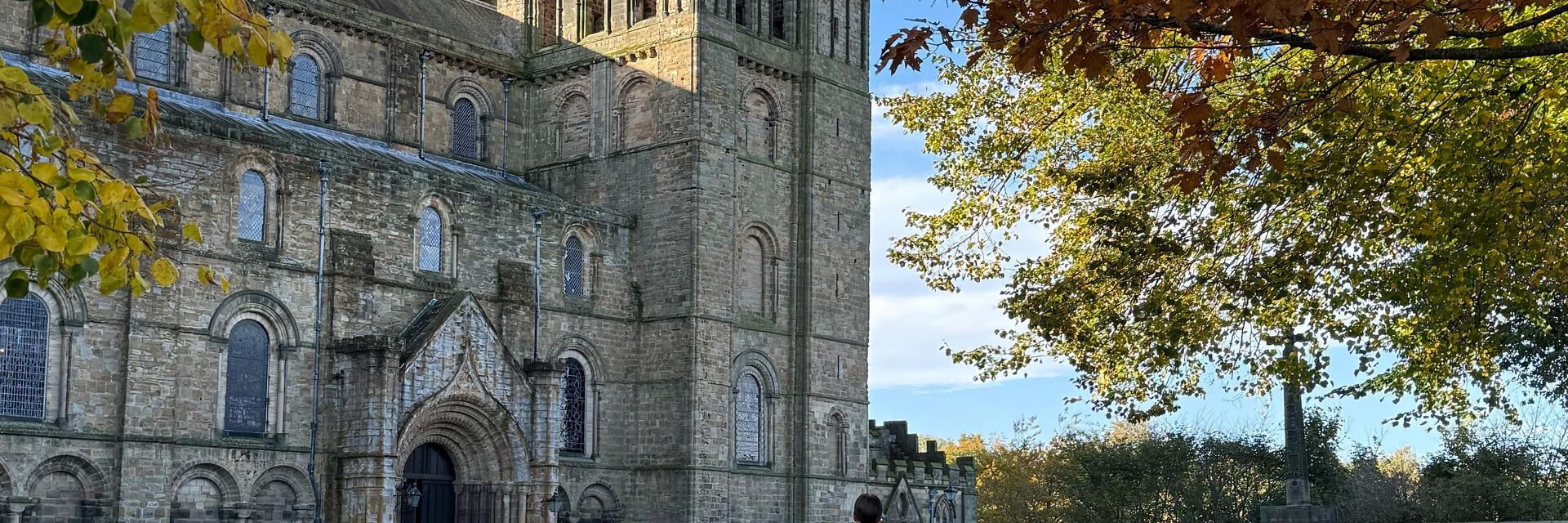 A woman in a warm jacket facing a large cathedral and tower.