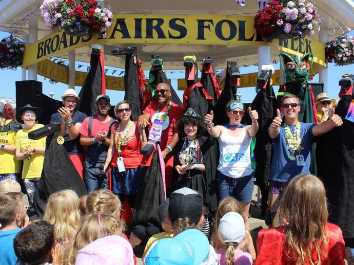 Crowd looking at people posing under a bandstand, with a banner reading: Broadstairs Folk Week