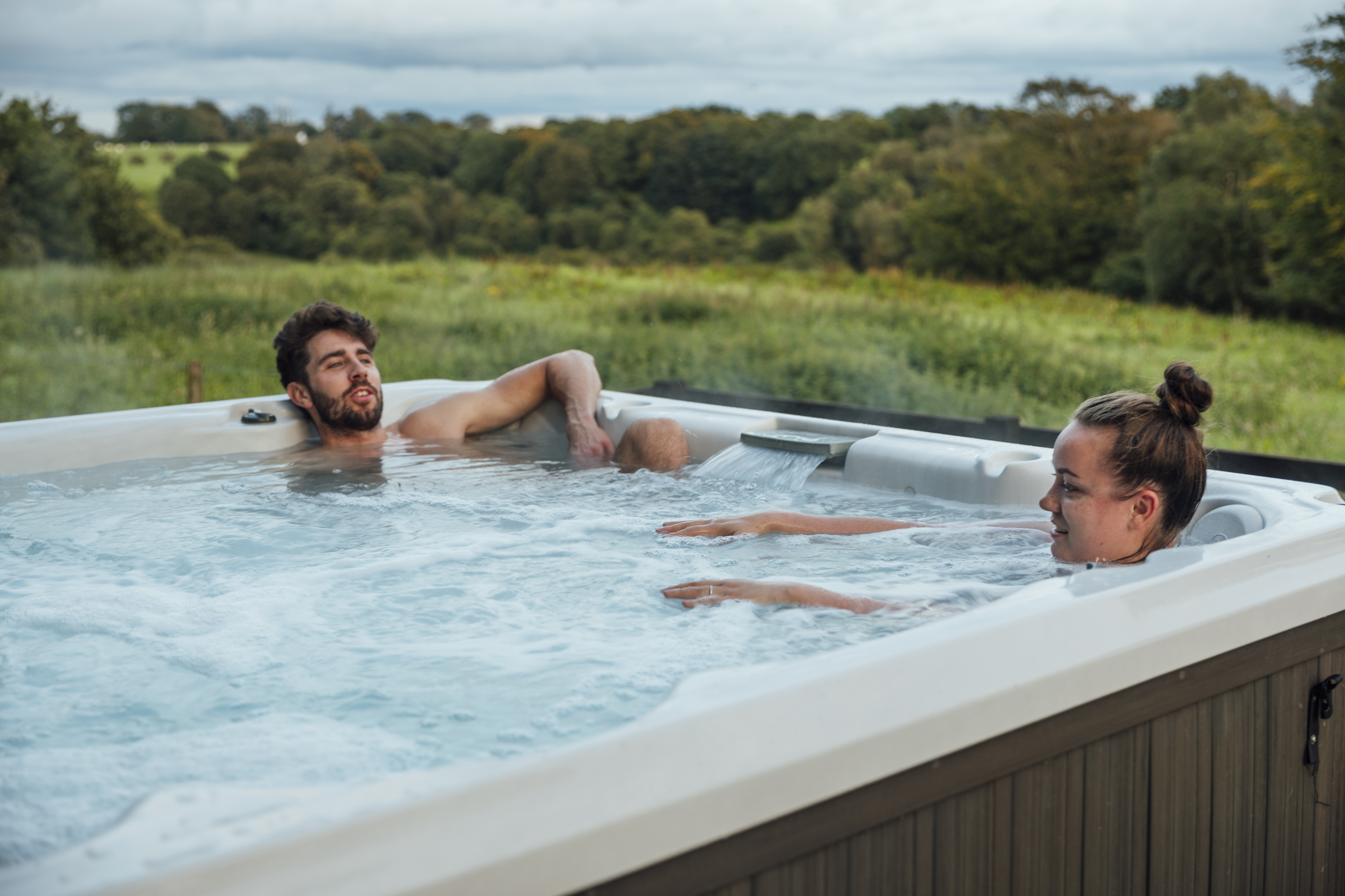 Couple relaxing in a hot tub overlooking countryside