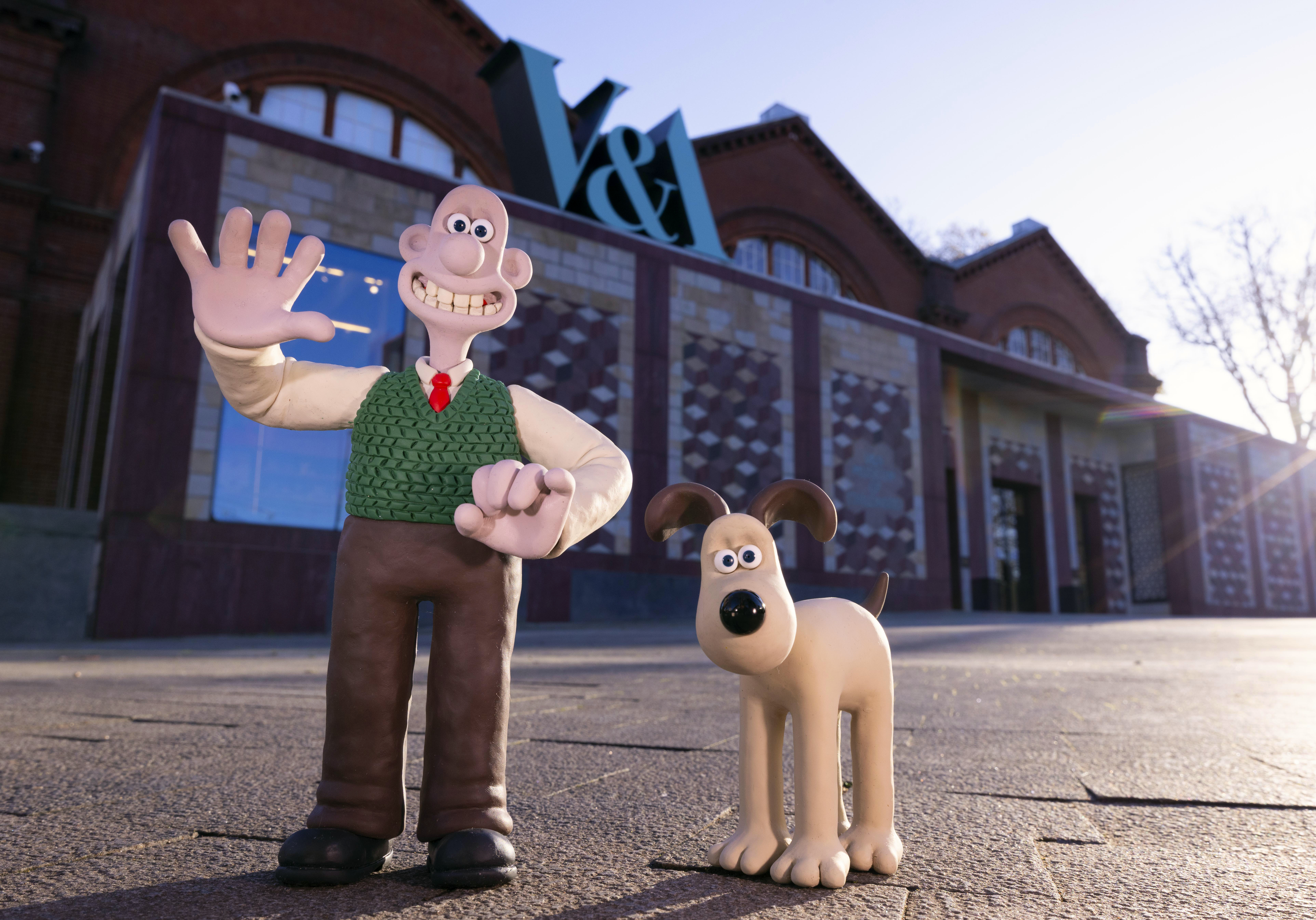 Clay animation characters stand outside a brick museum building with a large V&A sign, under clear sky.