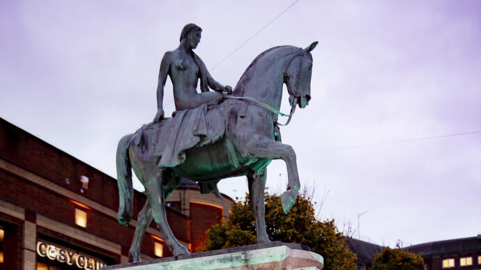 Two women standing in front of sculpture in a city