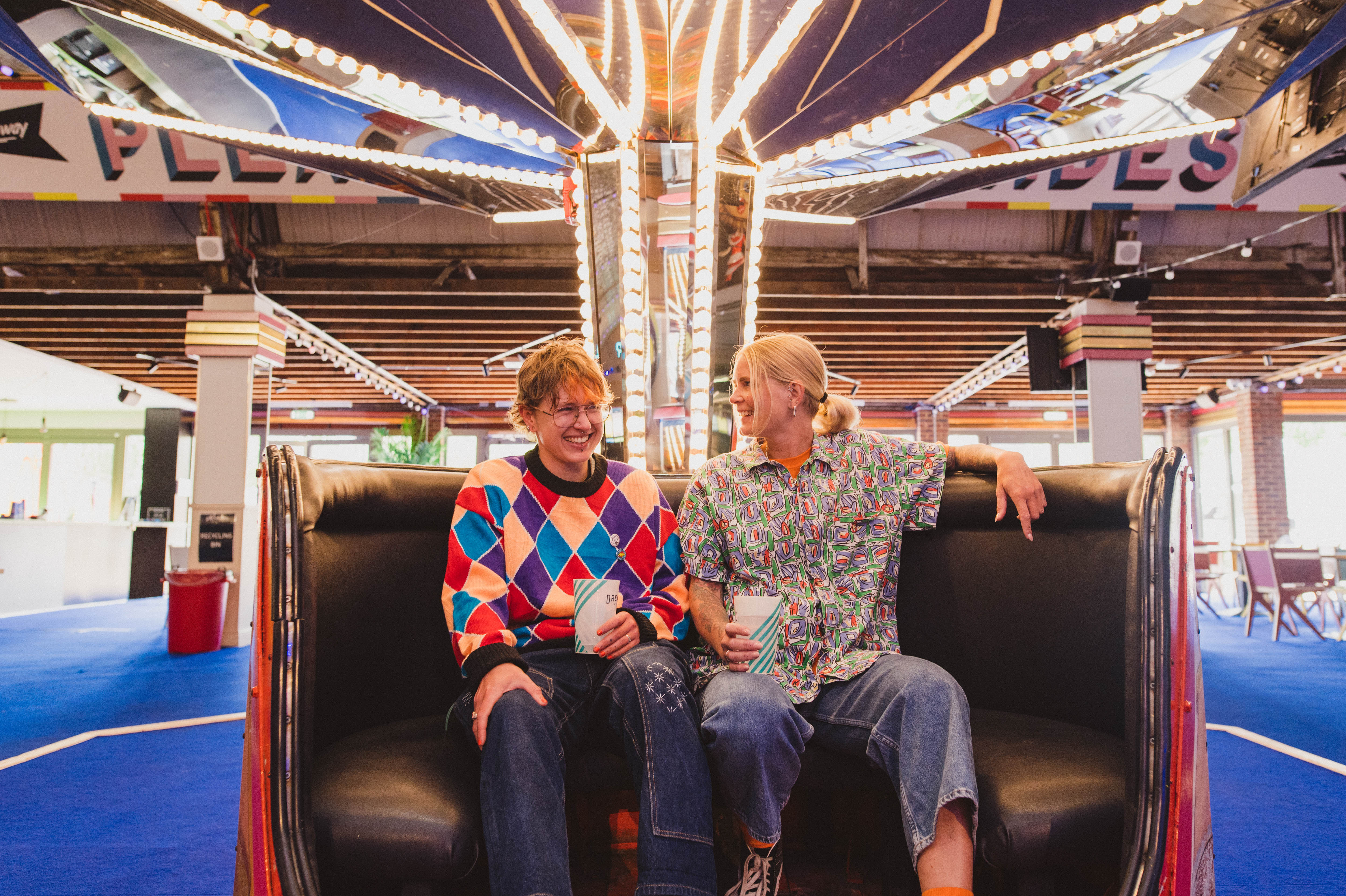 A man and a woman wearing roller skates sit in a retro teacup at a roller disco