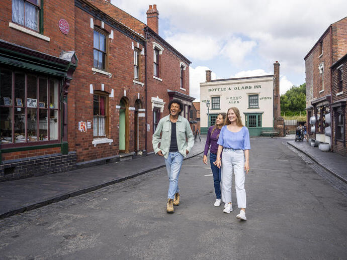 Three people walking and smiling in a historic-looking street with red brick buildings and a pub in the background.