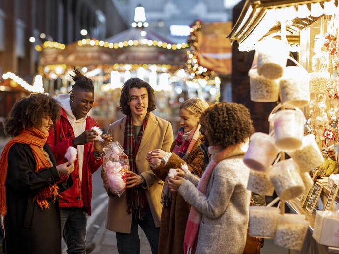 Grupo de jóvenes amigos compartiendo una bolsa de algodón de azúcar en el mercado navideño.