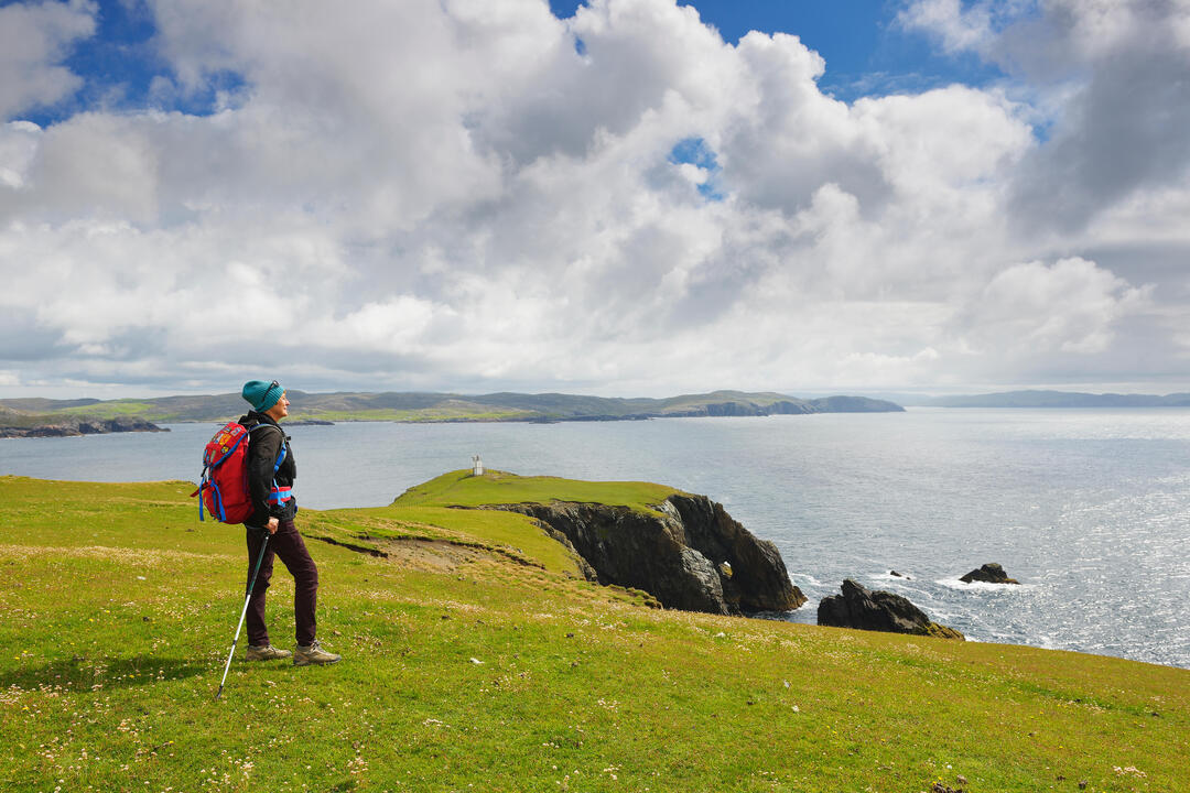 Woman stood on the top of a grassy cliff overlooking the sea