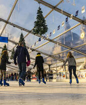 People ice skating on a skating rink under a glass ceiling