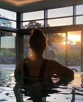 Une femme dans la piscine du Gaia Spa regardant par la fenêtre au coucher du soleil
