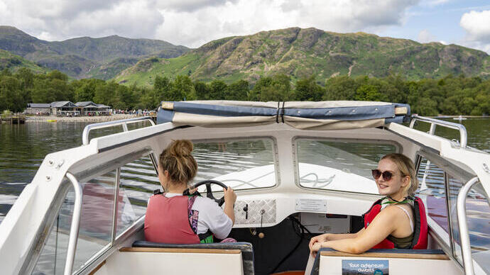 Town women sit ar the front of a boat on a lake with hills beyond