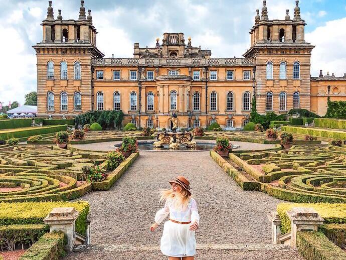Woman walking through the formal gardens in front of a palace