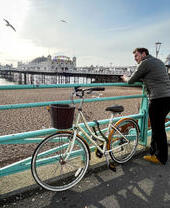 Mann, der mit einem Fahrrad an einem Geländer am Meer lehnt