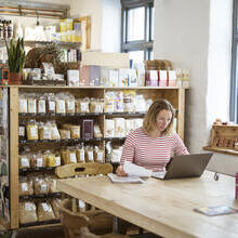 Woman in early 40s using laptop at a communal table in a health food shop and cafe