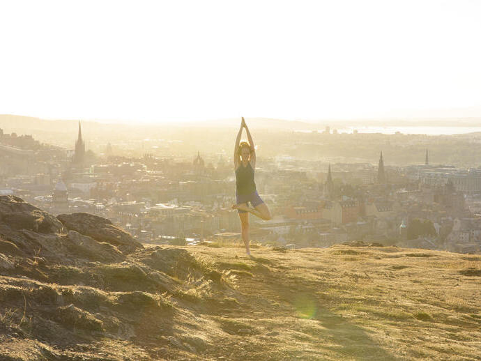 Young woman doing yoga on a hill overlooking a city