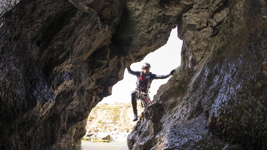 Gente practicando coasteering en Stair Hole, en los acantilados de piedra caliza a lo largo de la costa jurásica, cerca de Lulworth Cove, en Dorset. Gente escalando las rocas.