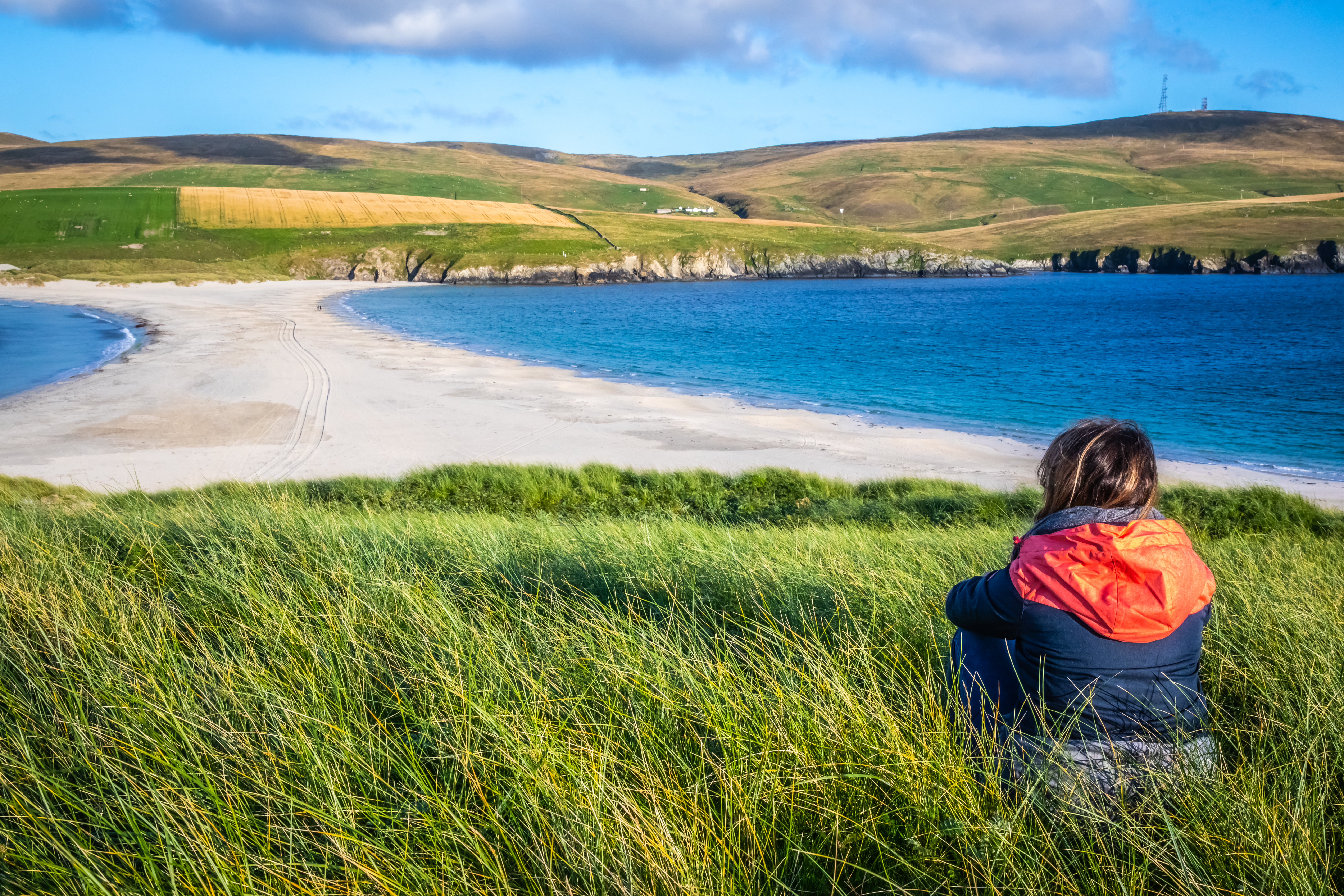A woman sitting in grass overlooking a spit and fields