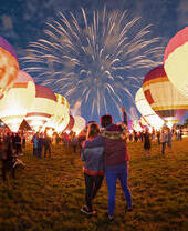 Couple watching grounded hot air balloons and fireworks in the night sky