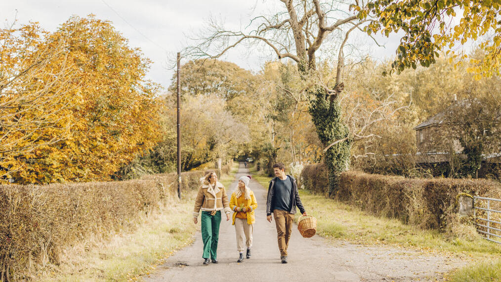 Two women and a man walking on a country lane in autumn