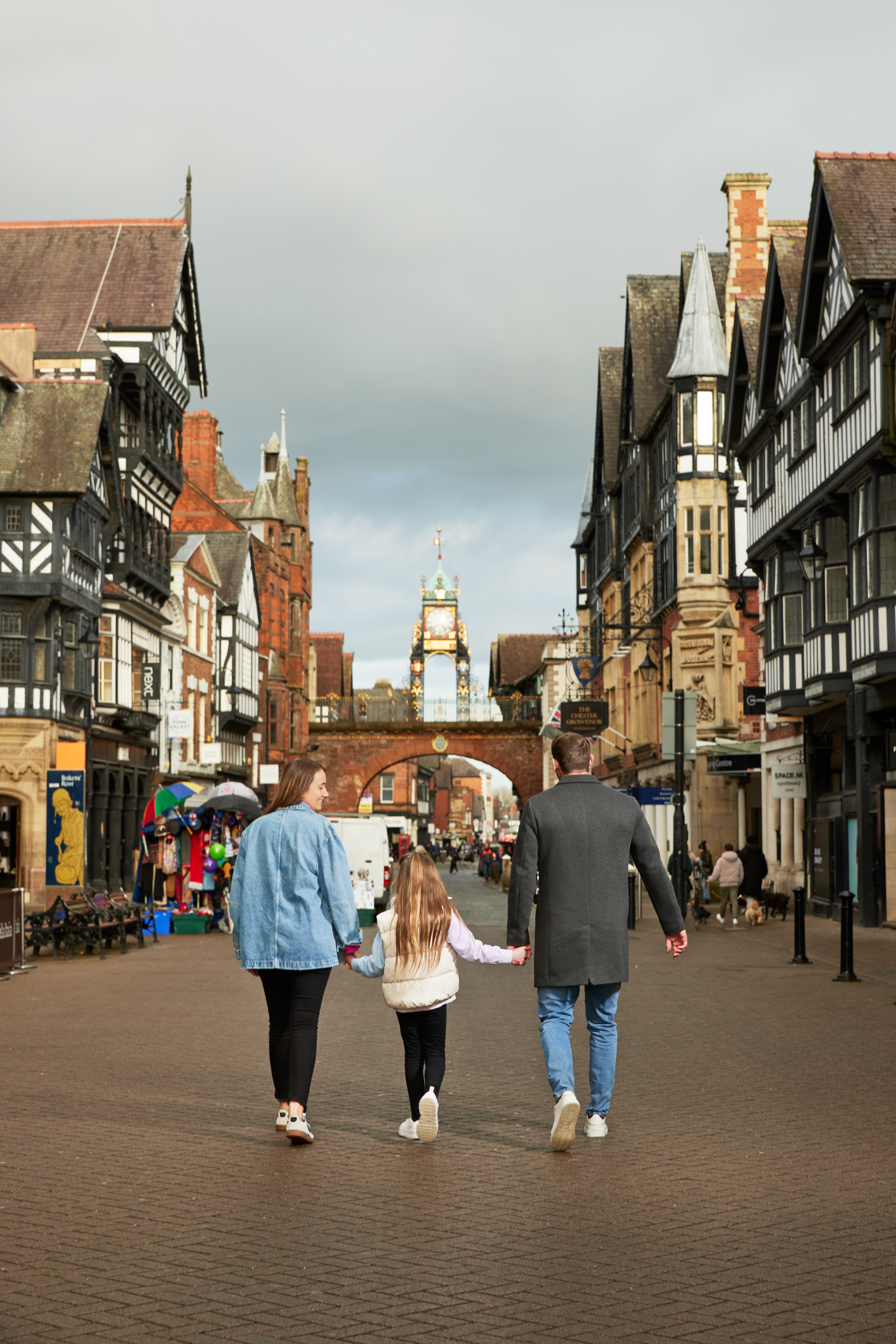 A family of three in front of the town clocktower in a shopping strip.