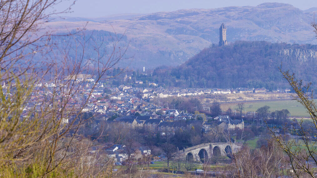 Aerial view of a town with a hilltop statue in the background.