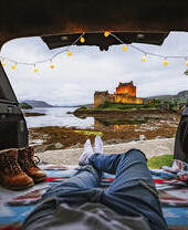 Mann liegt in einem Wohnmobil und schaut auf eine Burg in der Ferne