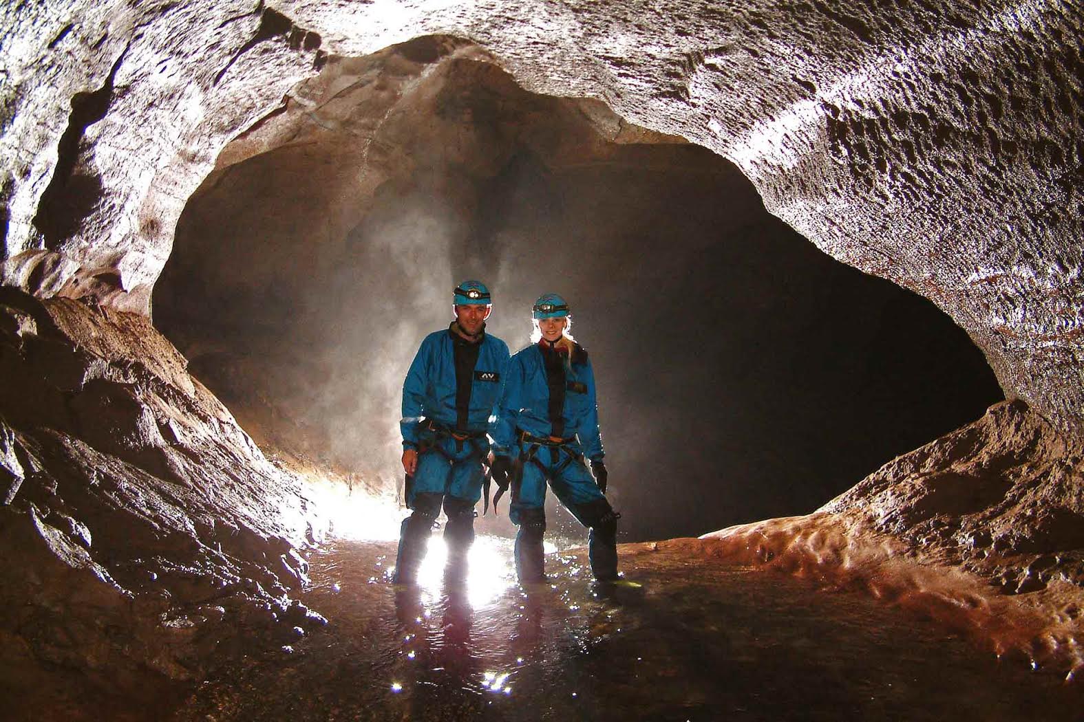 A couple standing in ankle-deep water within a back lit cave