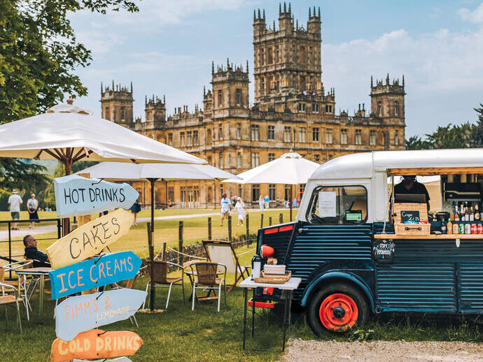 A food truck, parasols and direction signs in the ground of a castle