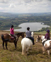 Un groupe de cavaliers sur une colline surplombant des terres agricoles et un lac.