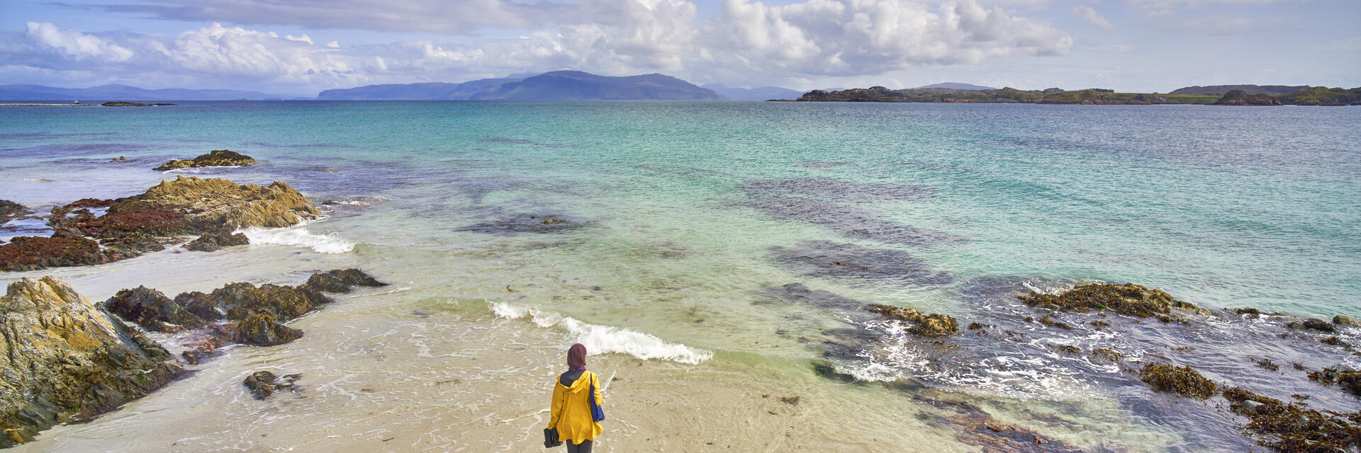 Eine junge Frau, die auf dem weißen Sandstrand mit kristallklarem, blauem Wasser spazieren geht.