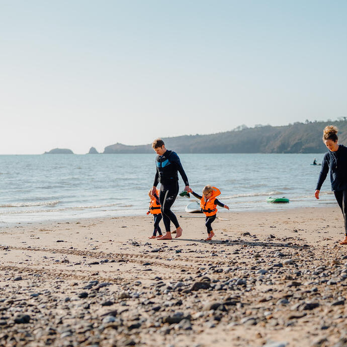 عائلة تمشي على الشاطئ، الرجل بصحبة طفلين صغيرين والمرأة تحمل لوح تزلج على شاطئ سوندرسفوت