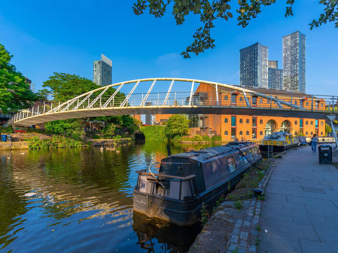 Canal boat moored on a canal with a pedestrian bridge and city buildings behind