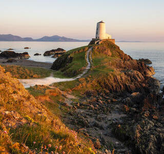 A path leading to a lighthouse on a prominent rocky outcrop by the sea