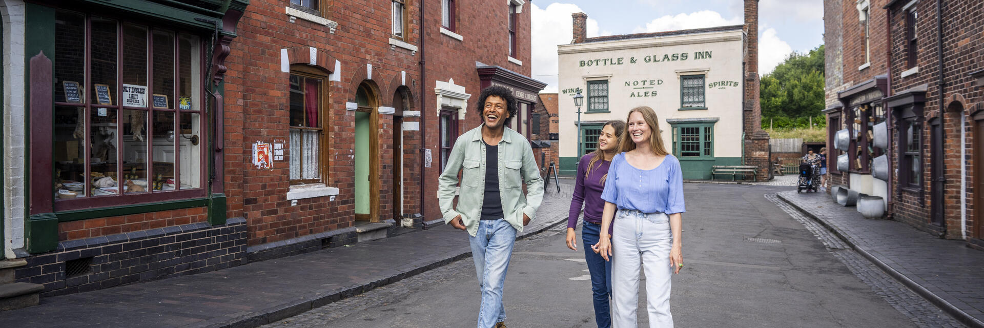 Three people walking and smiling in a historic-looking street with red brick buildings and a pub in the background.