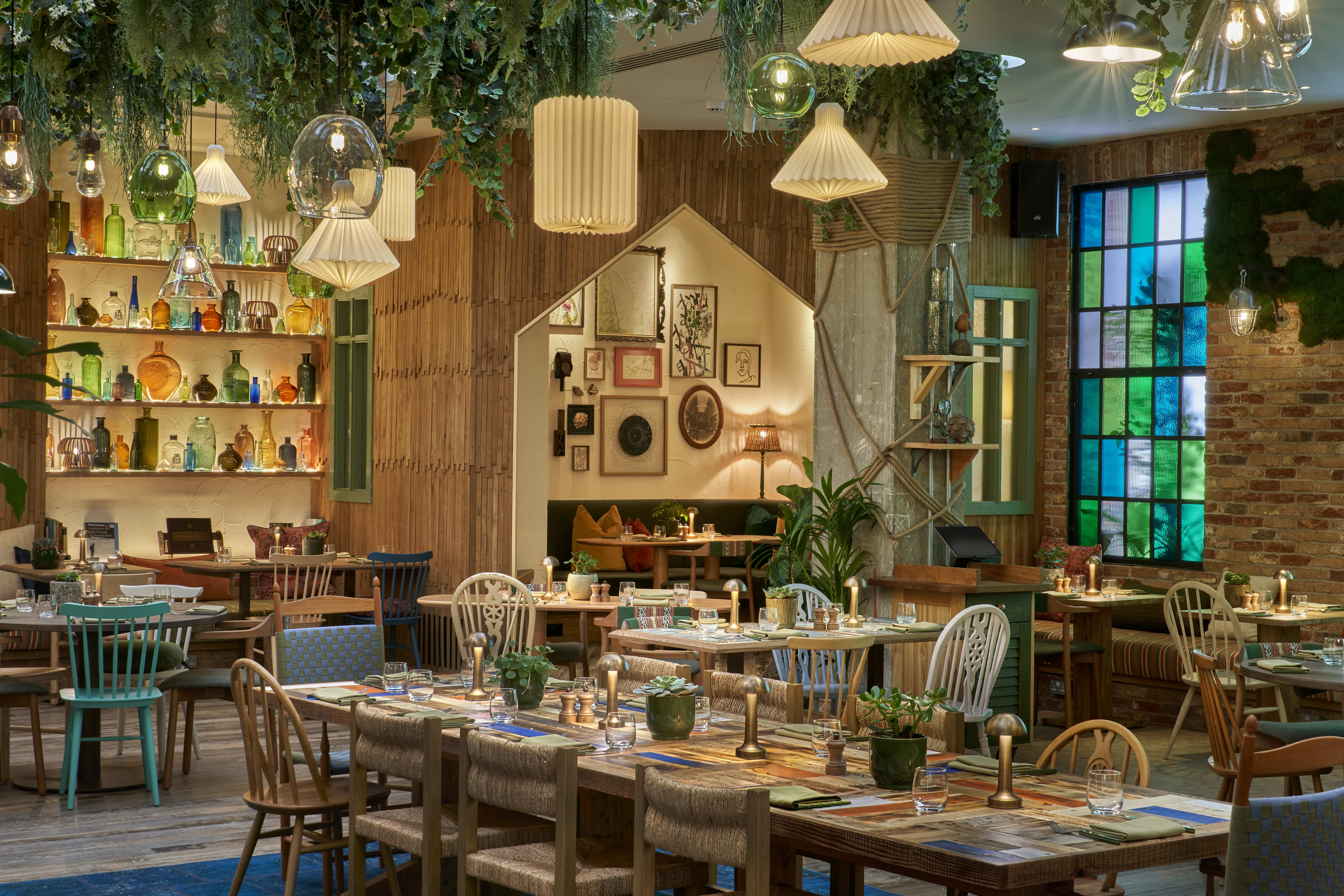 Tische in einem Restaurant mit Hängelampen und grünem Laub.