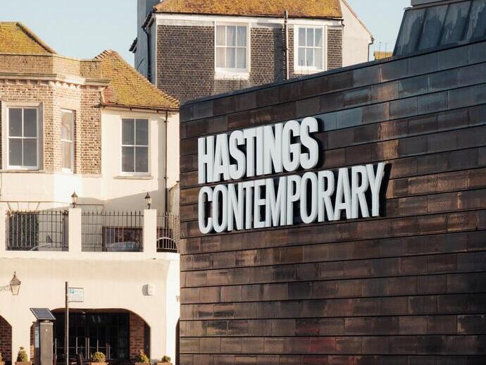 Exterior of a contemporary art gallery with modern facade and historic buildings in background under clear sky.