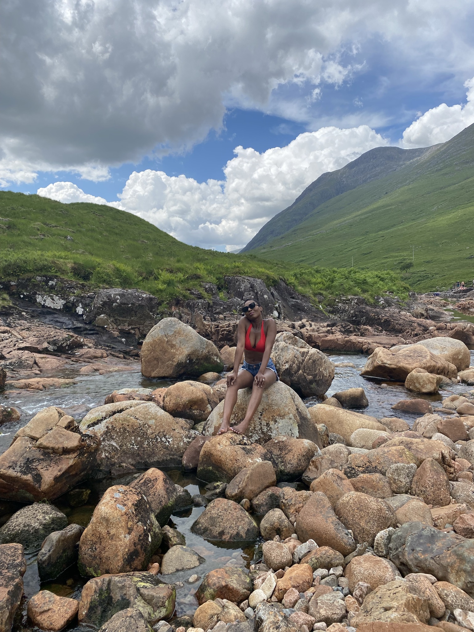Femme assise sur un rocher dans un ruisseau entouré de montagnes