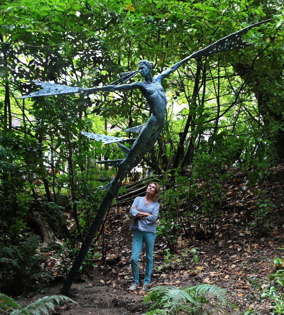 A lady observing a sculpture outdoor surrounded by trees