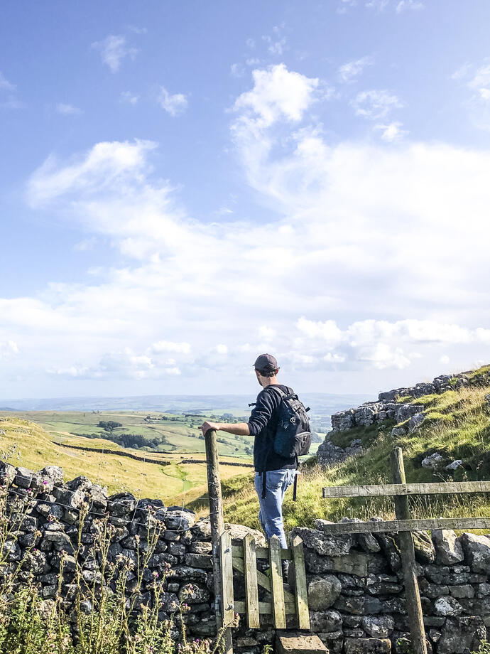 Man standing on stile over stone wall looking at landscape