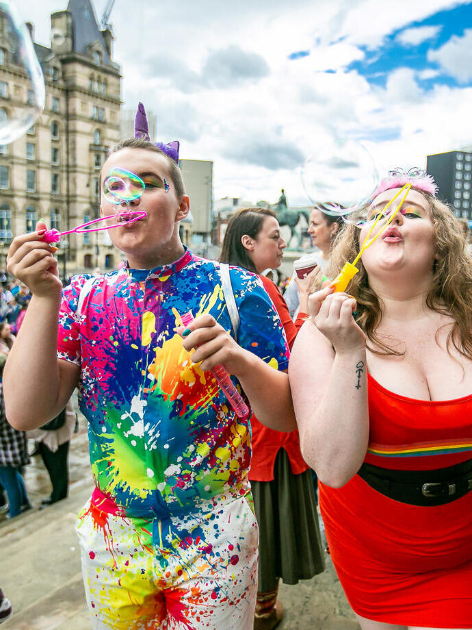 Two people celebrating Liverpool Pride by blowing bubbles towards the camera