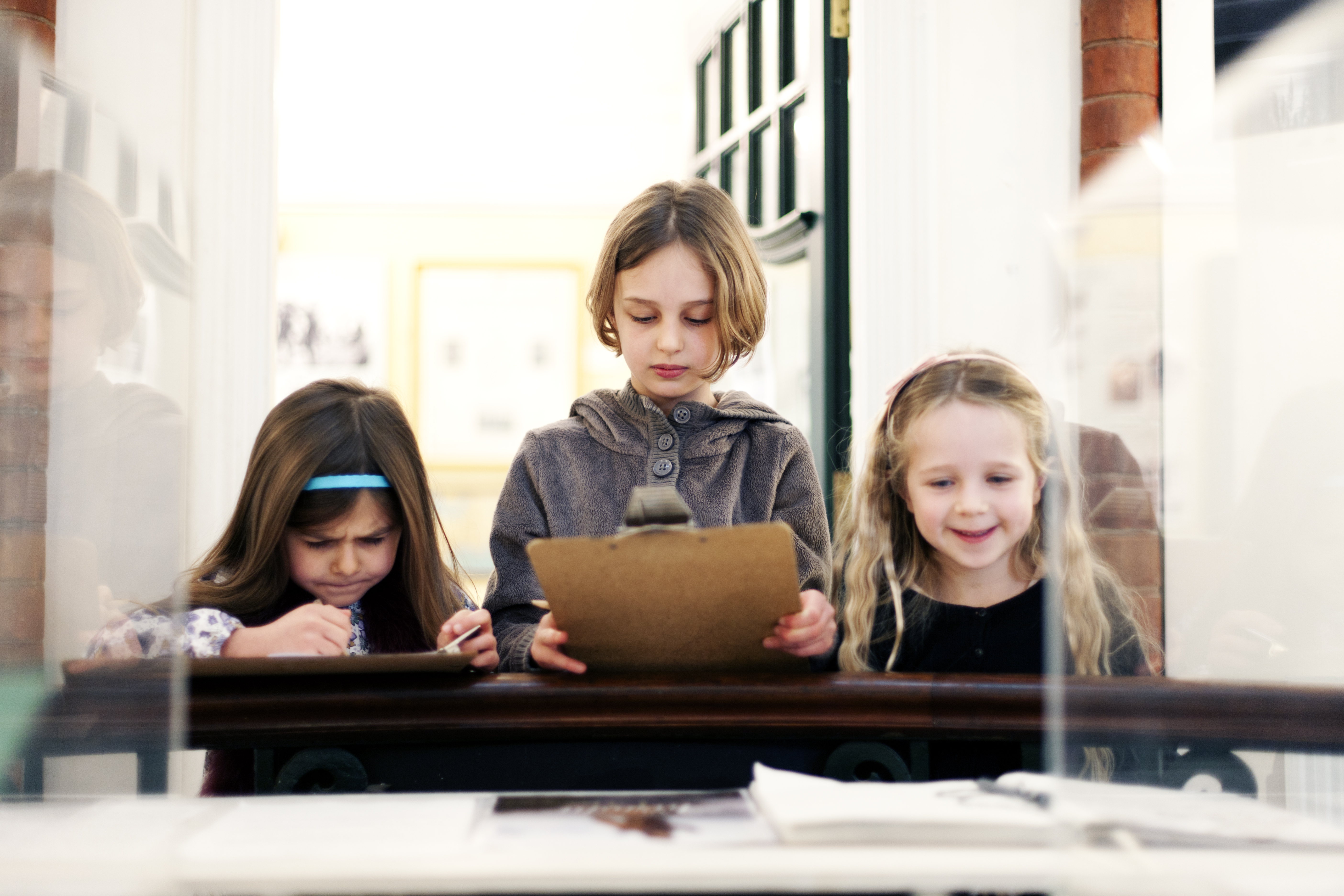 Three young girls study an exhibit in a glass display cabinet, in a museum.