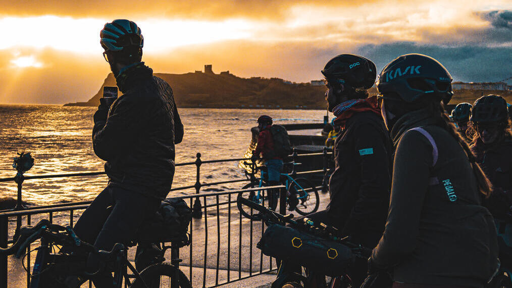 A group of cyclists taking a picture of the sunset on the coast