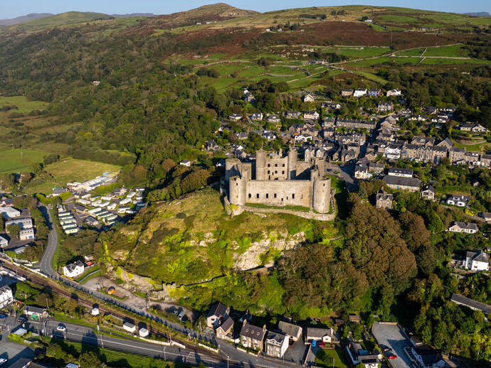 Aerial view of castle standing on a grassy hilltop surrounded by town and landscape