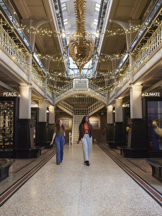 Two women talking, laughing visiting the prehistoric exhibition inside a large museum.