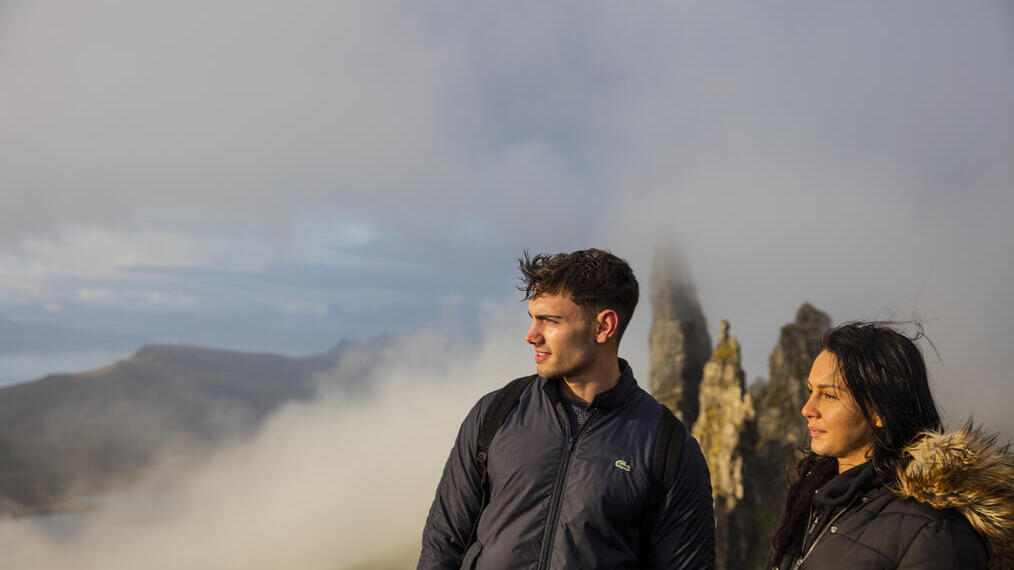 Couple standing near basalt pinnacles, watching mist