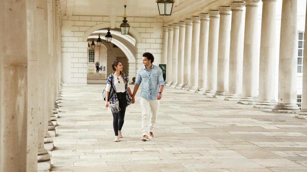 A hand in hand couple walking through marble colonnades.