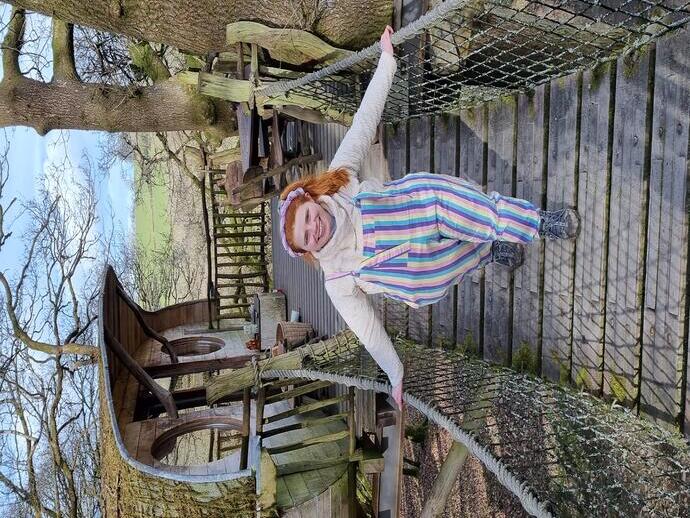 Giovane donna che attraversa un ponte di corda da una casa sull'albero in legno