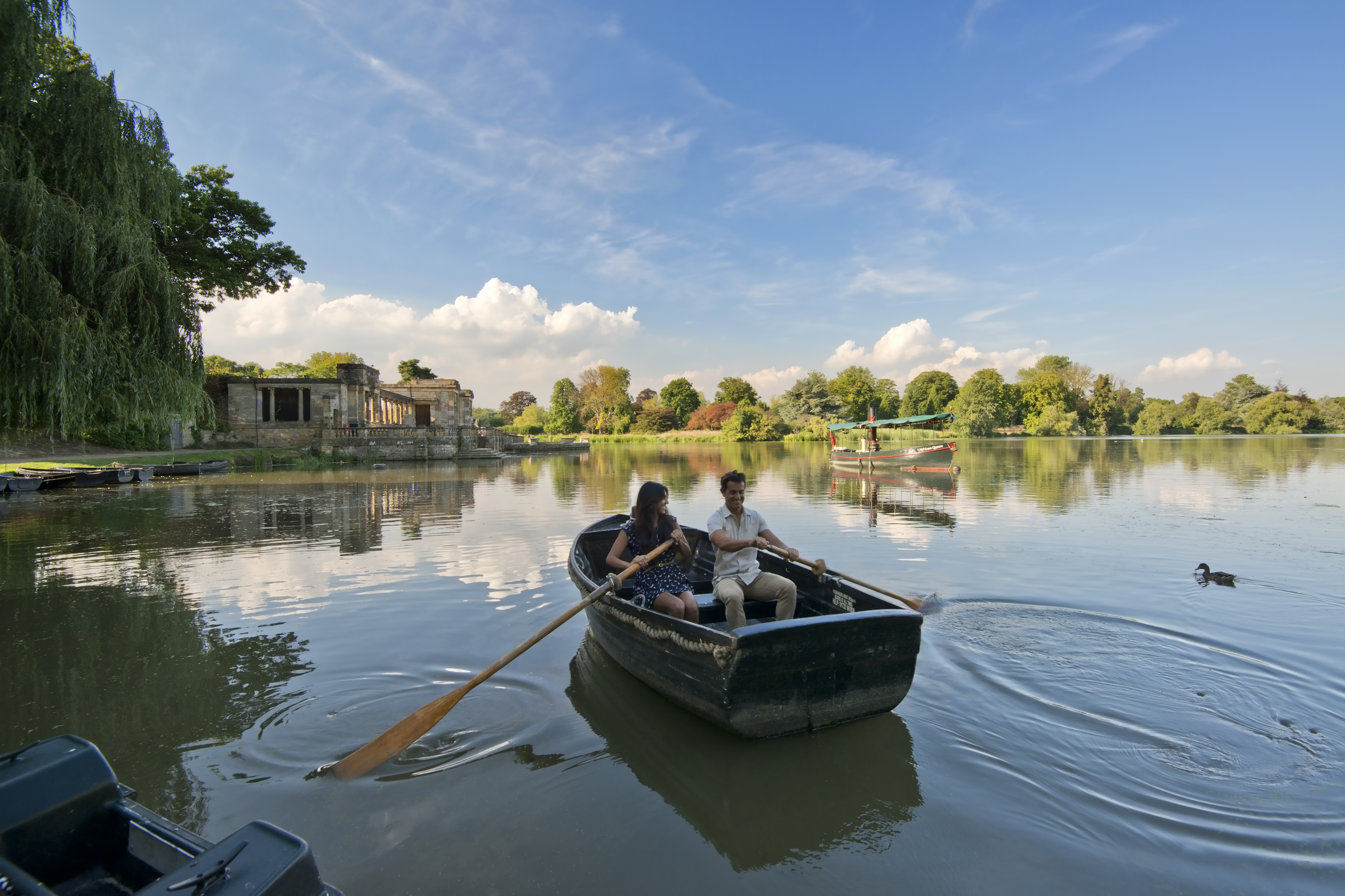 A man and woman in a rowing boat, rowing in still waters