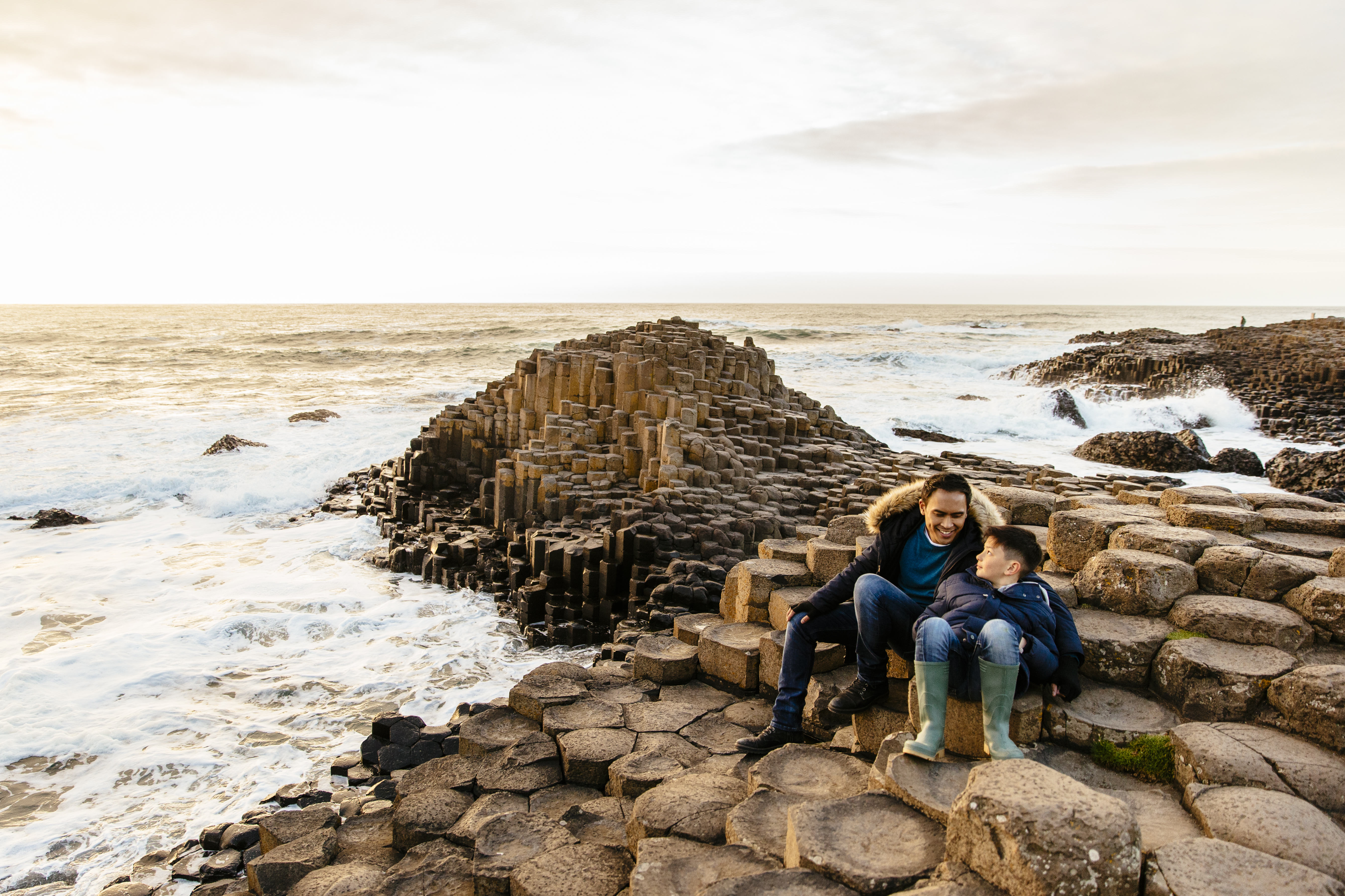 Man and child sitting on rock formations by the sea